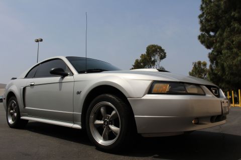 2002 Ford Mustang - A silver 2002 Ford Mustang GT is parked outdoors under a clear sky, showing its distinctive hood scoop and GT badging.