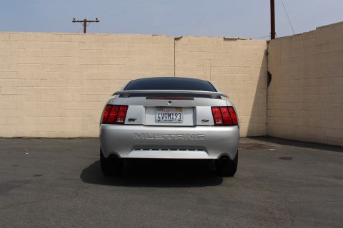 2002 Ford Mustang - Rear view of a silver 2002 Ford Mustang GT parked in front of a beige brick wall.