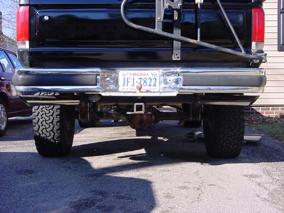 Black pickup truck rear with Virginia license plate JFJ-7822 and hitch receiver. Another vehicle is parked to the left