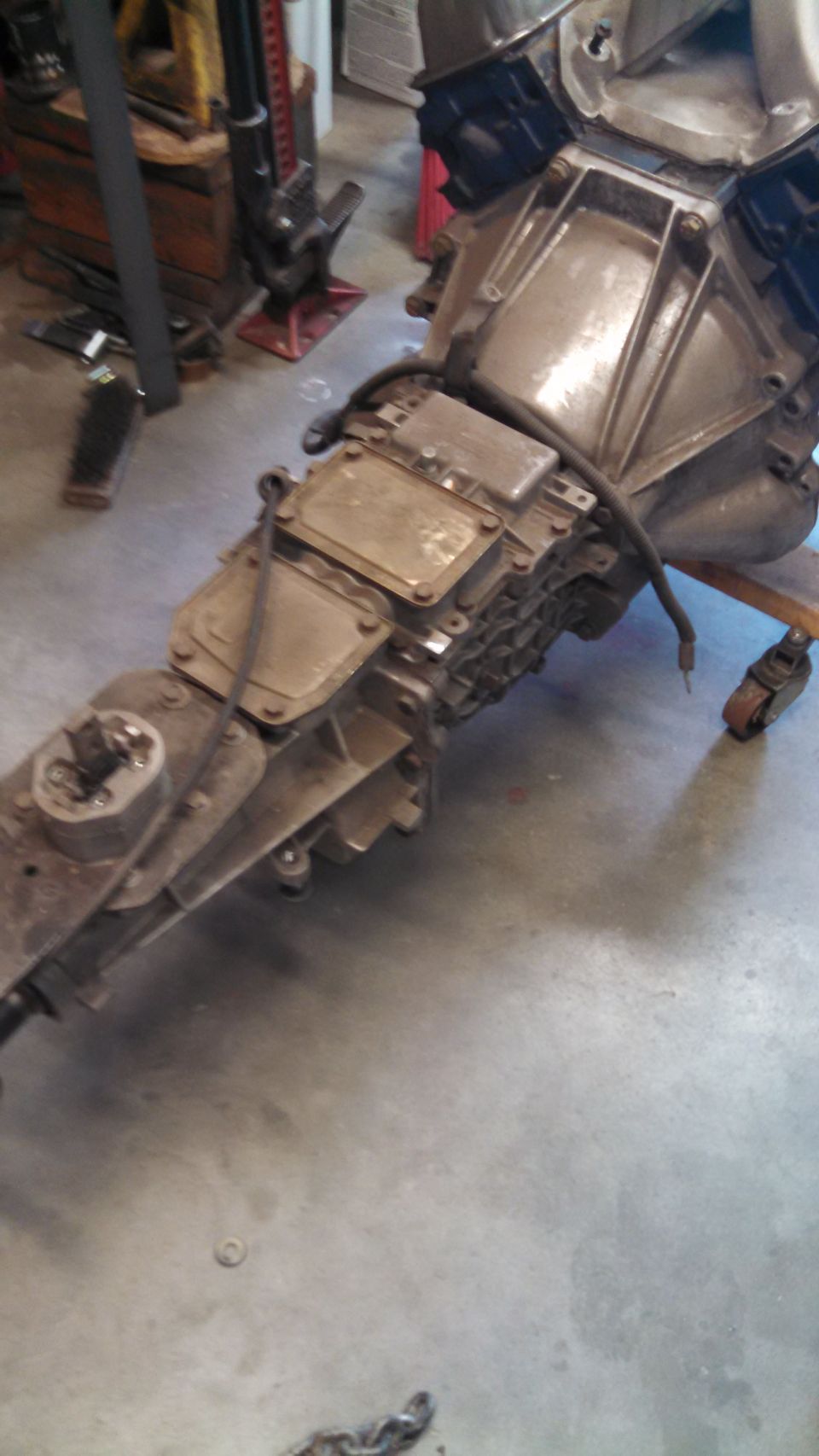 Engine and transmission assembly on a stand in a garage. There's a red jack in the background