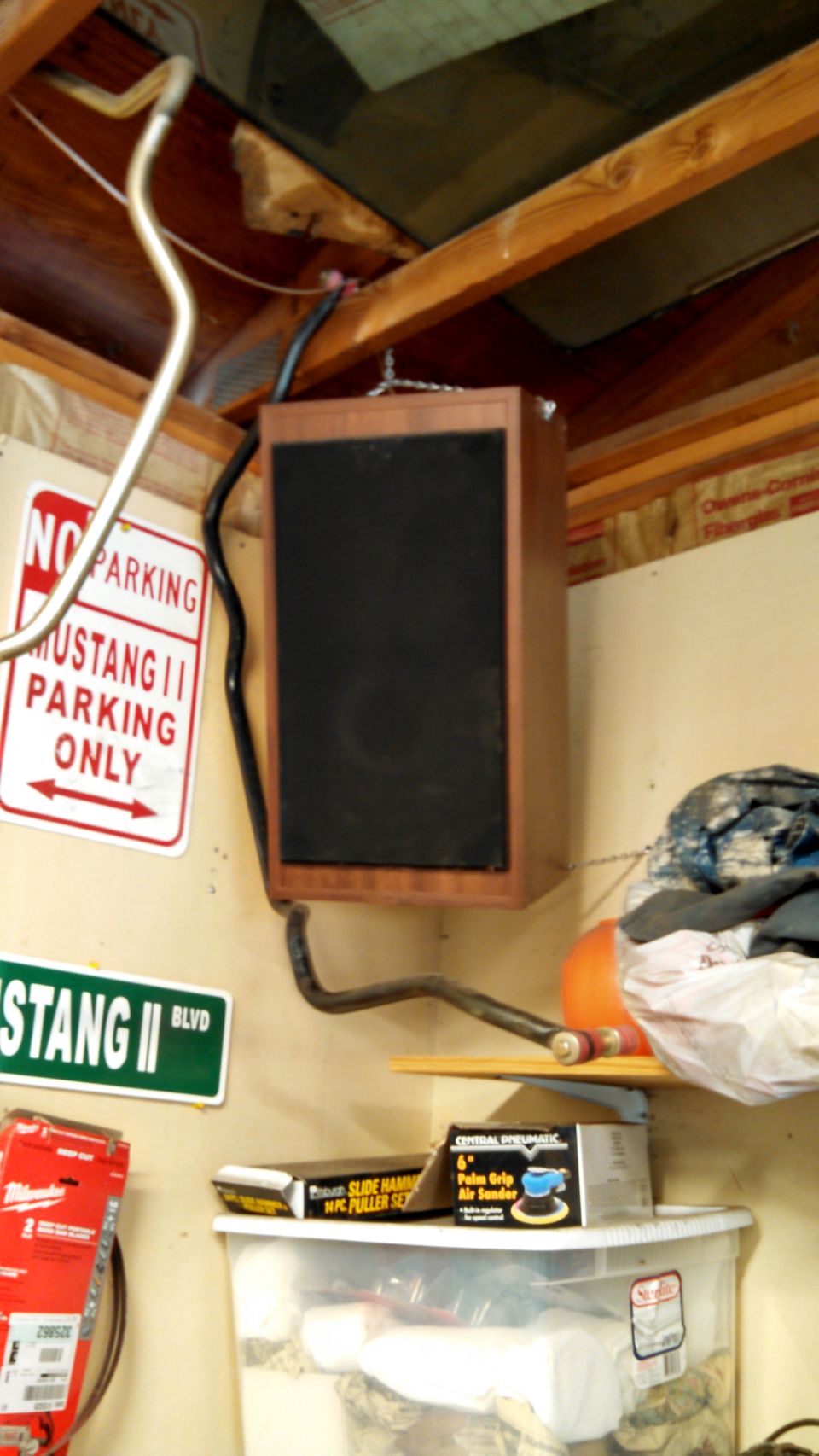 Speaker mounted from ceiling with 'NO PARKING MUSTANG II PARKING ONLY' and 'MUSTANG II BLVD' signs on wall