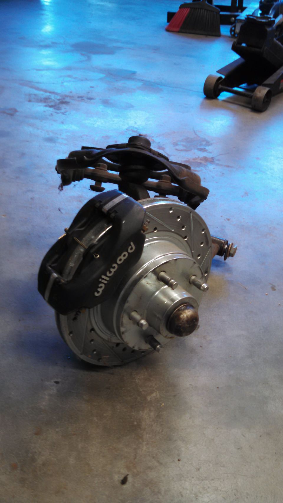 Front brake assembly with Wilwood caliper and drilled rotor on concrete floor
