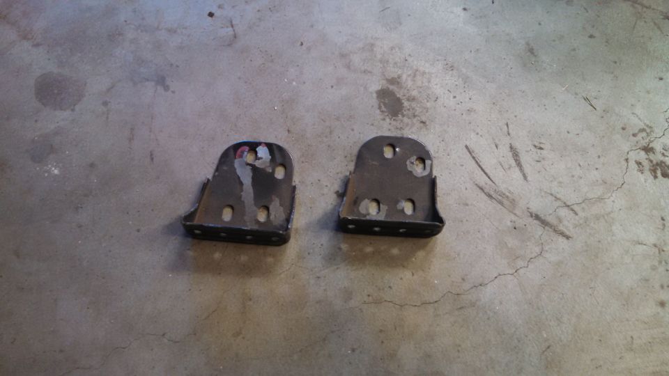 Two metal brackets with multiple bolt holes, lying on a concrete floor