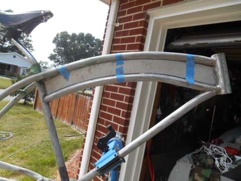 bicycle frame with blue tape holding a textured panel in place, parked outside a brick garage