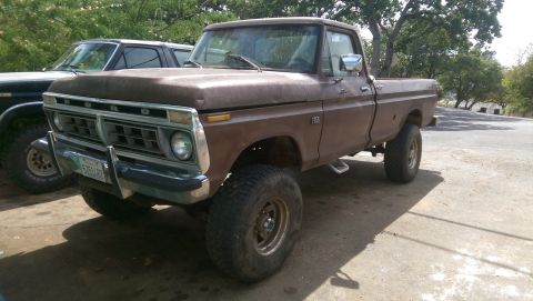 1976 Ford F-250 - This brown Ford F-150 pickup has a lifted suspension and is parked next to another truck.
