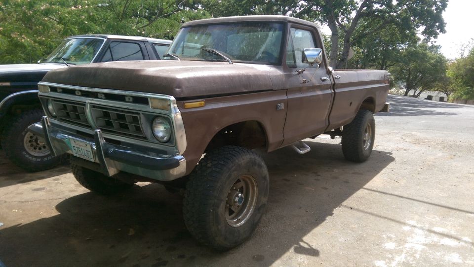 Brown 1975 Ford F-150 pickup truck with lifted suspension, parked next to another truck