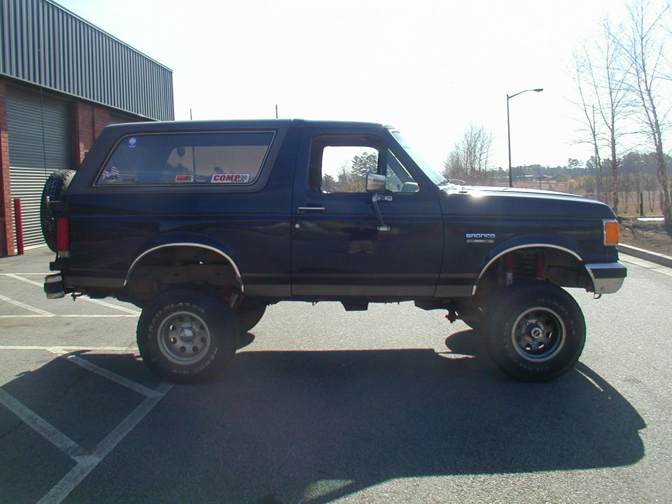 Dark blue 1988 Ford Bronco with lifted suspension and off-road tires parked outside a building