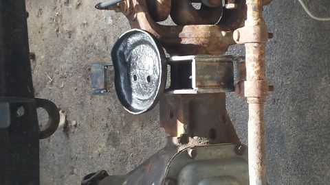 Close-up of a rusty metal part, possibly from a vehicle's suspension, with a Supermotors logo at the bottom ri