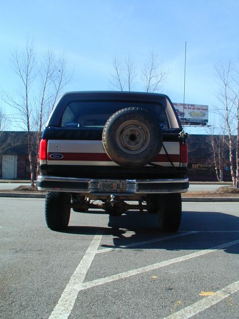 1988 Ford Bronco - Rear view of a black Ford Bronco with a spare tire on the tailgate, parked in a lot.