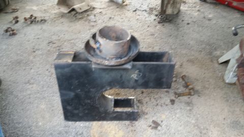 Welded metal bracket with a pipe on top, on a concrete floor with bolts scattered nearby