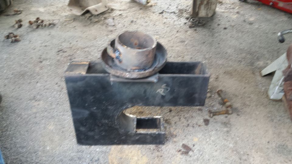 Welded metal bracket with a pipe on top, on a concrete floor with bolts scattered nearby