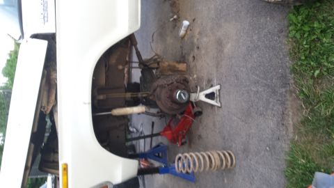 White vehicle's front suspension disassembled with jack stands and a removed coil spring on the ground