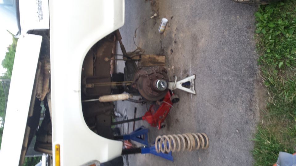 White vehicle's front suspension disassembled with jack stands and a removed coil spring on the ground