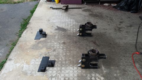 Four metal brackets and a long tool laid out on a concrete surface