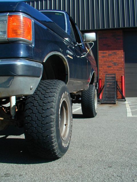 1988 Ford Bronco - This lifted 1988 Ford Bronco features prominent off-road tires and a high suspension, viewed from a low front-quarter angle.