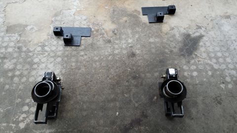 Two shock absorbers and two mounting brackets laid out on concrete