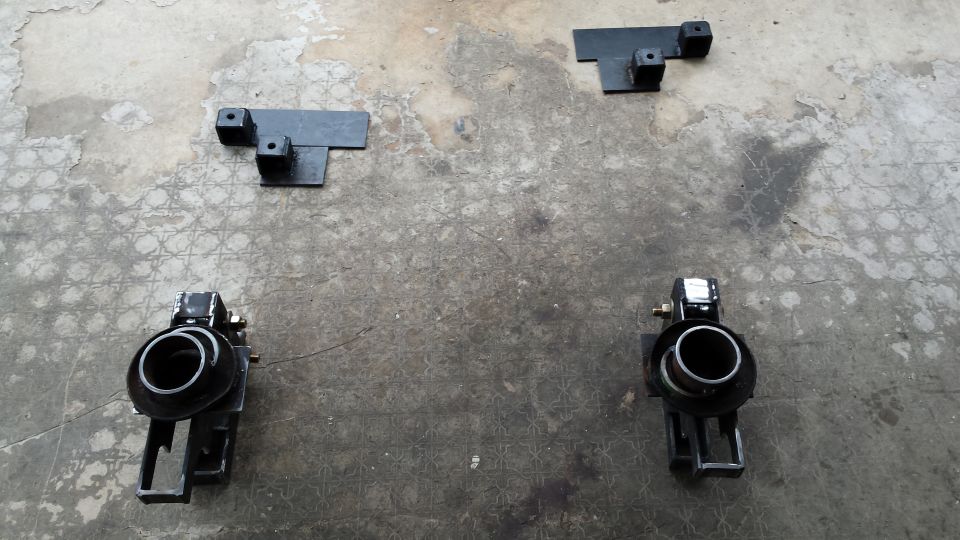 Two shock absorbers and two mounting brackets laid out on concrete