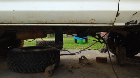 Underside of a white vehicle, showing suspension, exhaust, and tires. Some rust is visible on the body