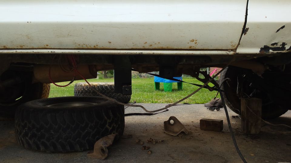 Underside of a white vehicle, showing suspension, exhaust, and tires. Some rust is visible on the body
