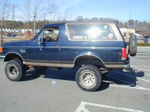 1988 Ford Bronco - Side view of a lifted 1988 Ford Bronco, showing its blue paint and tan trim.