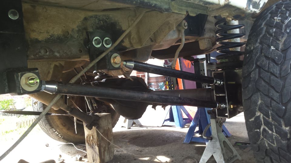 Underside of a vehicle showing suspension arms, springs, and differential. The vehicle is on jack stands