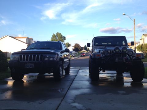 2004 Jeep Grand Cherokee - Two Jeep SUVs, a Grand Cherokee and a Wrangler, are parked in a driveway under a blue sky.
