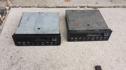 1995 Ford Bronco - Two car radios are displayed on a concrete surface, showing their front panels and top casings.