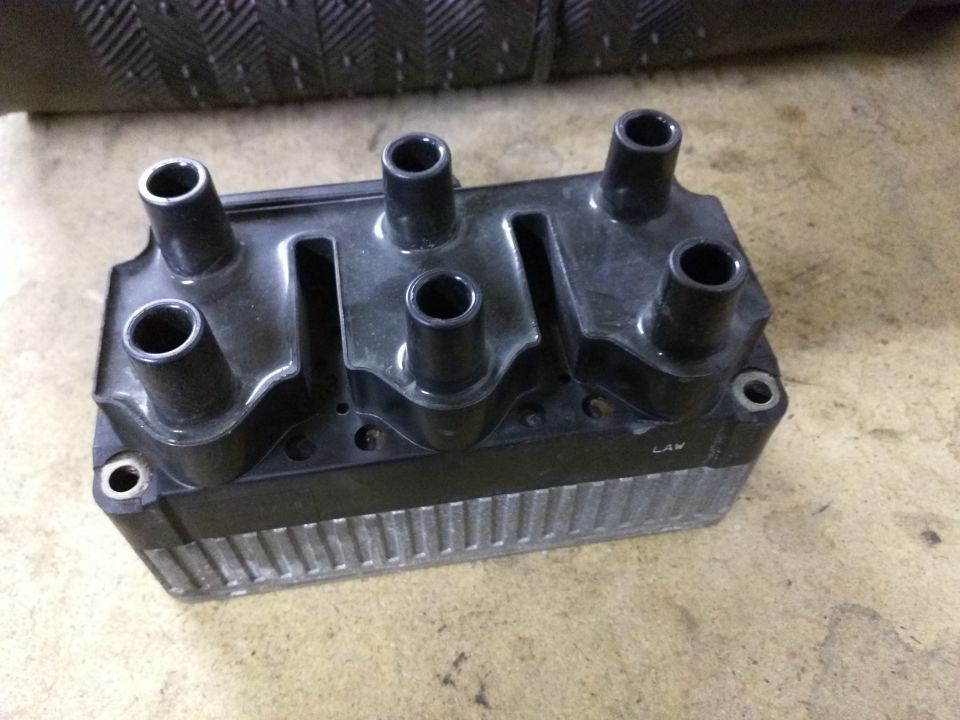 Ignition coil pack with four spark plug wire boots. Some text is visible on the side