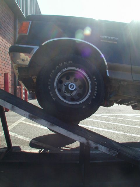 1988 Ford Bronco - Ford Bronco's front wheel and fender are visible as it is loaded onto a ramp.