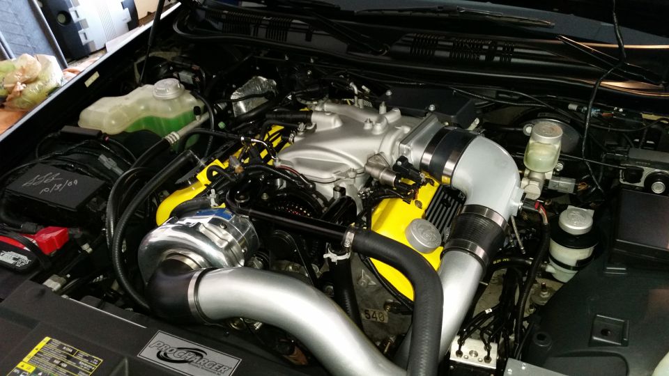 Engine bay with silver supercharger, yellow valve covers, and silver intake piping
