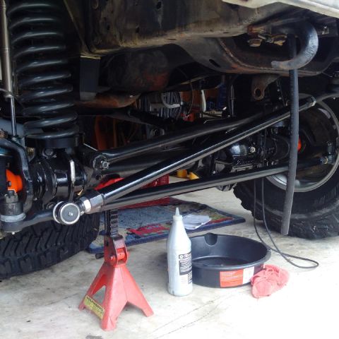 1978 Ford Bronco - The underside of a vehicle, likely a Ford Bronco, is shown supported by a red jack stand. Visible components include a large coil spring, s…