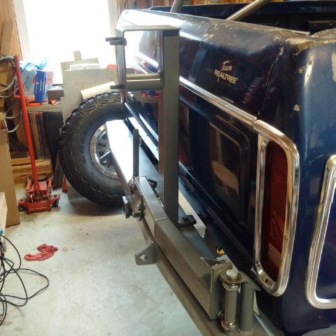 1978 Ford Bronco - A close-up rear view of a dark blue pickup truck bed with a custom-mounted spare tire carrier and a large off-road tire. The truck bed has…