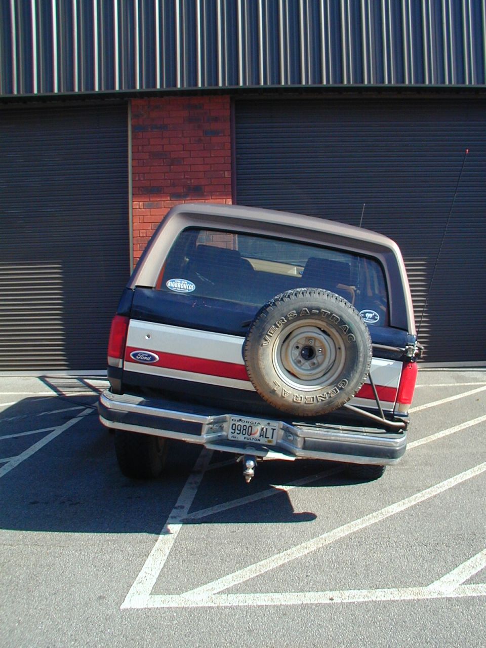 Rear view of a blue and tan Ford Bronco with a spare tire mounted on the back. License plate reads 9980 ALT