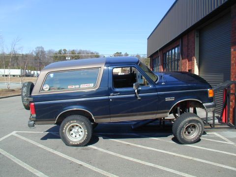 1988 Ford Bronco - This lifted Ford Bronco is positioned on a ramp, showing its side profile and spare tire.