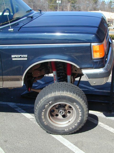 1988 Ford Bronco - A blue 1988 Ford Bronco is shown with its front fender and a lifted tire. The Bronco badge is visible on the side.