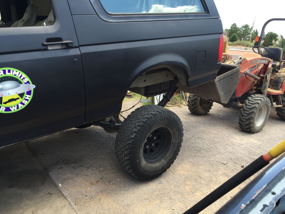 Matte black Ford Bronco with large tires, lifted, next to a red Case tractor.