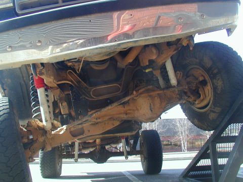 1988 Ford Bronco - The undercarriage of a 4x4 vehicle is visible as it sits on a ramp, revealing its suspension and mechanical parts.