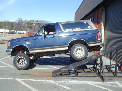 1988 Ford Bronco - A blue Ford Bronco is positioned on a ramp next to a building.