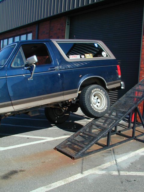 1988 Ford Bronco - A blue Ford Bronco with a tan top is partially on a metal ramp in front of a brick building.