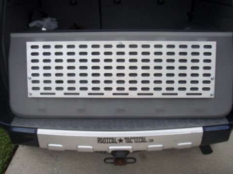 2005 Toyota 4Runner - The rear of a dark colored SUV shows a silver metal panel with a grid of oval cutouts mounted on the interior tailgate. A silver bumper wit…