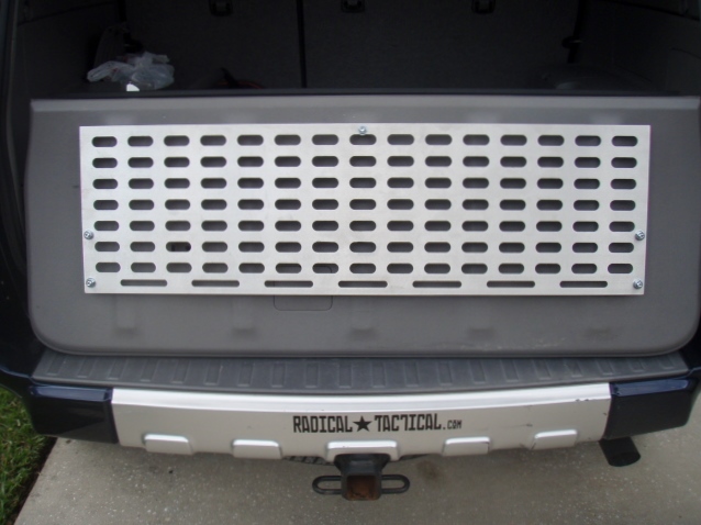 Rear of a dark SUV with a metal grid panel inside the tailgate and "RADICAL TACTICAL.COM" on the bumper.