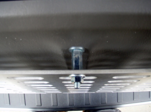 Close-up of bolts fastening a perforated metal plate to a vehicle's underside.