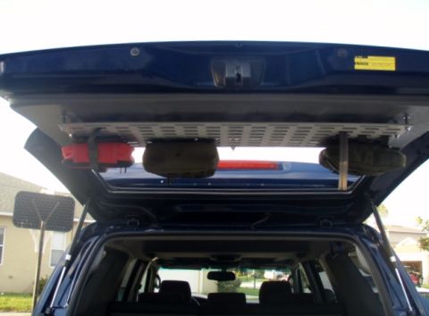2005 Toyota 4Runner - The open rear hatch of a dark blue SUV reveals a custom overhead storage rack installed in the cargo area. The rack holds two items: a pair…