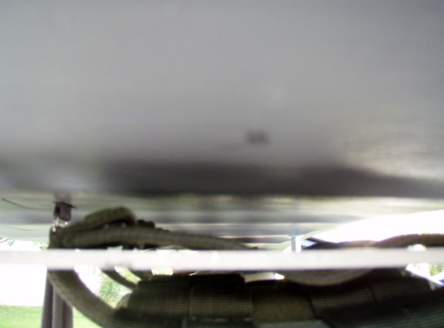 Underside of a vehicle showing a strap attached to a metal panel.