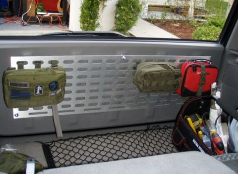 2005 Toyota 4Runner - The interior of a vehicle shows a metal panel mounted on the back wall, with three pouches and a red first-aid kit attached. A cargo net is…