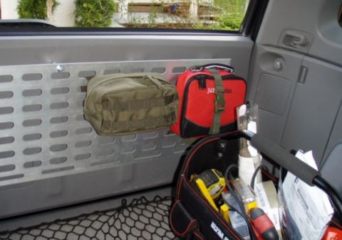 2005 Toyota 4Runner - The interior cargo area of a vehicle shows a silver perforated panel mounted to the side wall. Two bags, one olive green and one red, are a…