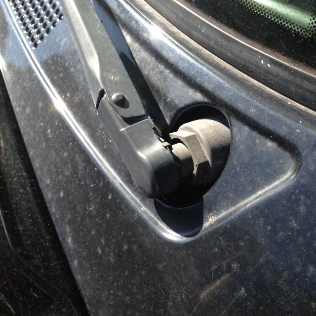 Close-up of a dusty black car windshield wiper arm and base.