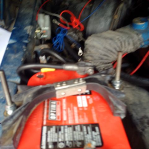 1978 Ford Bronco - A close-up view of a red Optima battery with visible red and blue wiring connected to it. The battery is secured with a metal clamp and is…