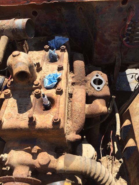 1946 Jeep Willys - A close-up view of a heavily rusted engine block with a spark plug installed. Blue cloths are stuffed into two of the spark plug holes.