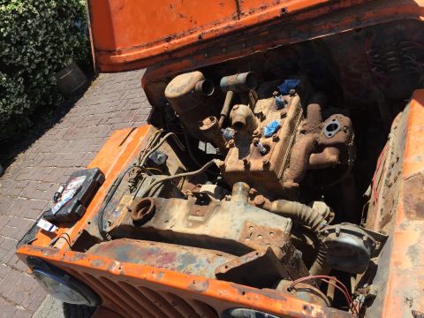 1946 Jeep Willys - The engine bay of an orange vintage Jeep is shown, with the hood open, revealing a rusty engine and various components. Tools and a toolbox…